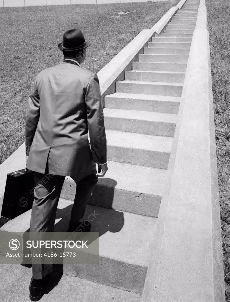 1960S Business Man In Suit & Fedora Holding Briefcase Starting Up Long Flight Of Cement Stairs Ahead Of Him