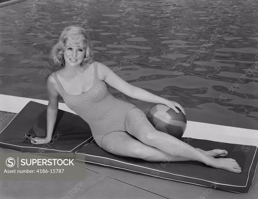 1960S Smiling Blond Woman Wearing Swimsuit By Pool Posing Hand On Beach Ball  