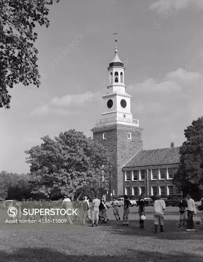 1950S School Football Team Practicing On Lawn In Front Of Stone Campus Building With Clock Tower