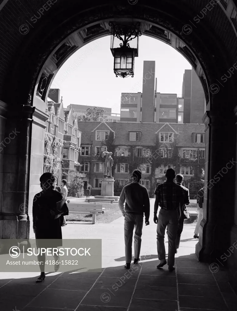 1960S College Students Walking Through Archway In Campus Building With Quadrangle In Background