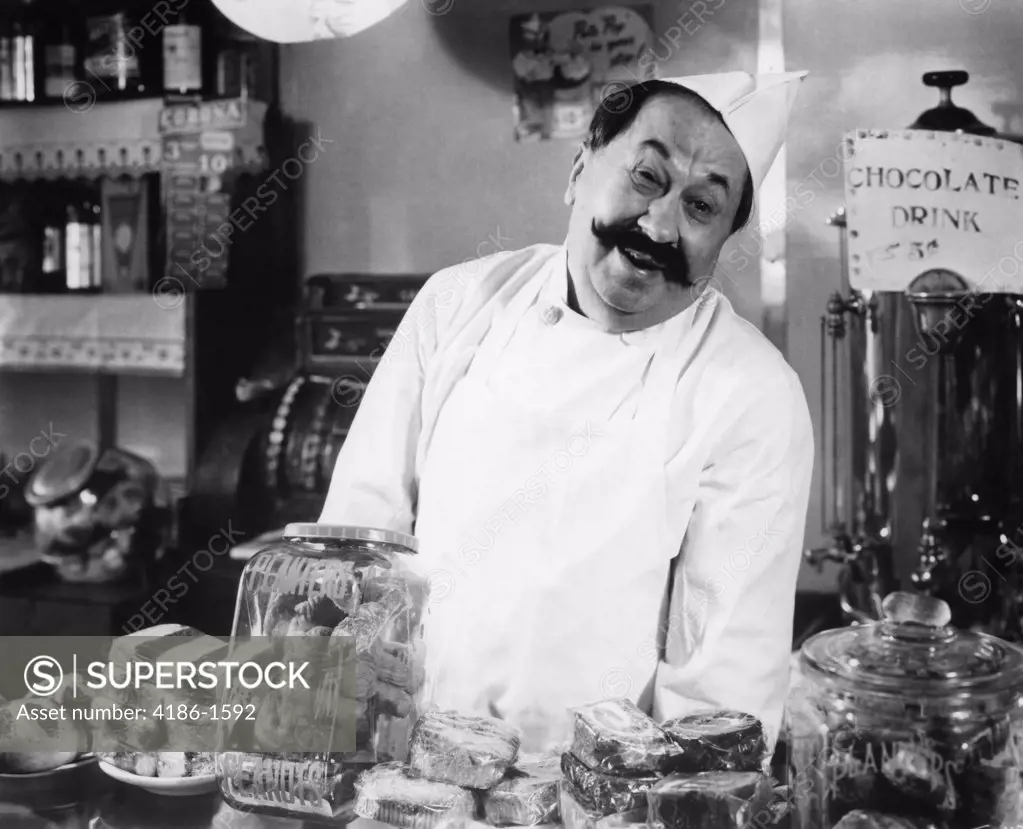 Vintage Portrait Of Smiling Proprietor Behind Counter In General Store