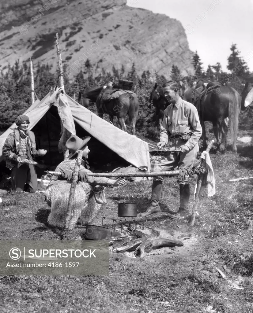 1920S 1930S Two Men And One Woman Eating A Meal Around A Campfire With A Tent And Horses At Baker Lake Alberta Canada