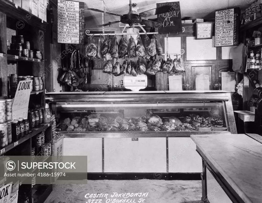 Old-Time Butcher Display Case With Meat Hanging On Rack Above In Small Grocery Store