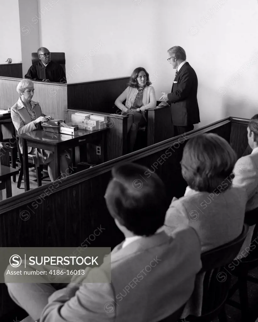 1970S Courtroom Scene Female Witness Being Questioned While Jury Looks On Indoor