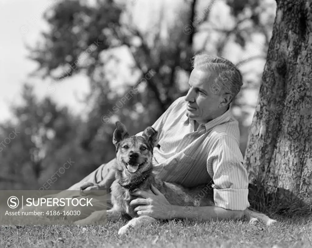1930S 1940S Elderly Man Lying Under A Tree With Dog Leisure Relax Retire Yard Grass Shade