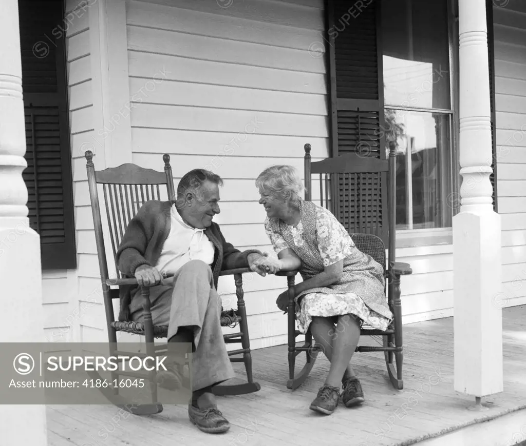 1970S Elderly Couple In Rocking Chairs On Porch Holding Hands
