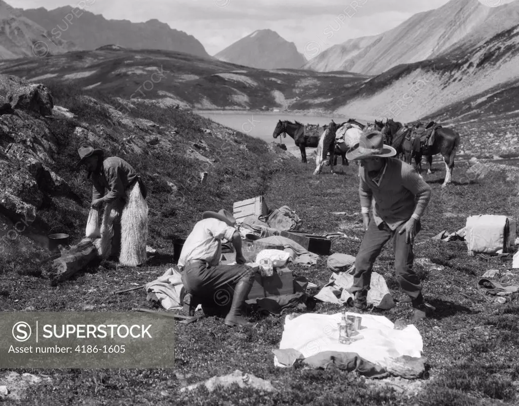1920S 1930S Three Men Cowboys At Campsite Preparing Food Horses In Background Alberta Canada