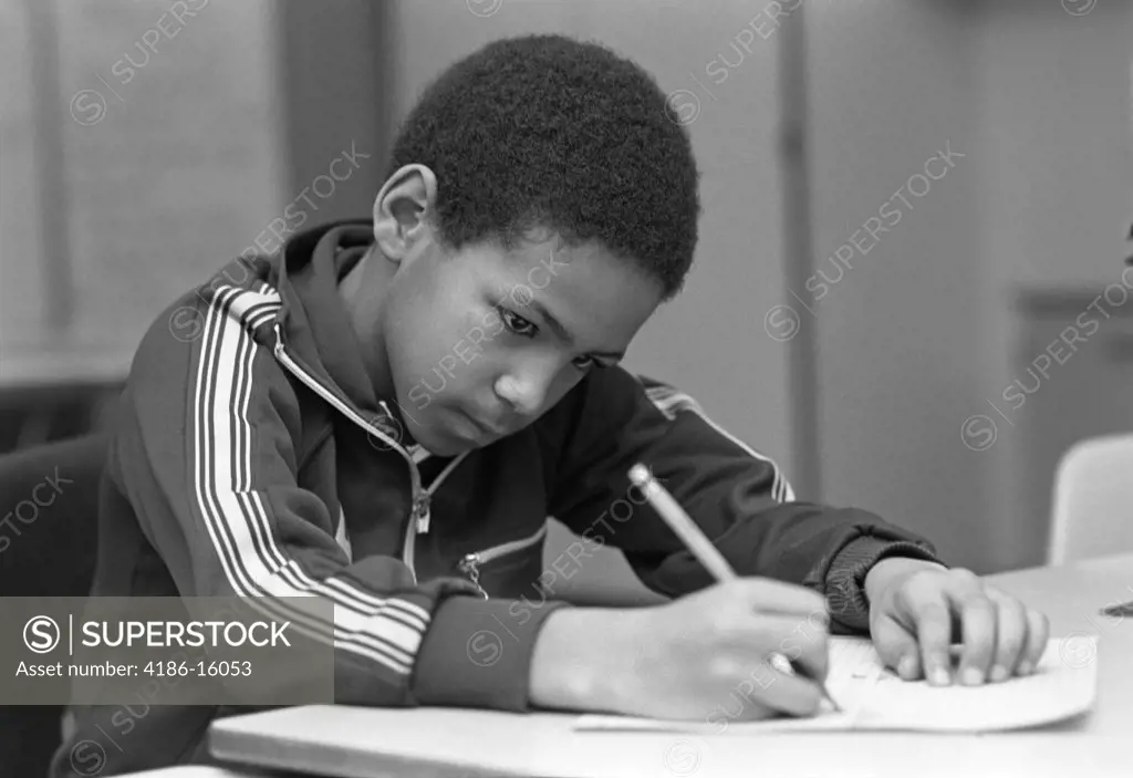 1980S African American Male Grade School Student Sitting At Desk In Classroom Writing