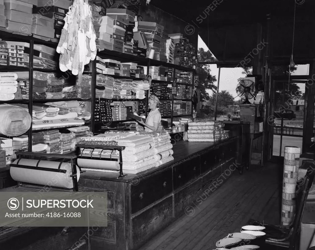 1940S Elderly Woman Pulling Merchandise From Shelf In Country Store