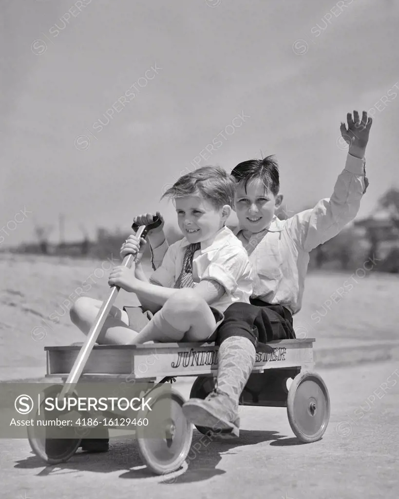 1930s TWO BOYS RIDING DOWN HILL IN JUNIOR ROADSTER WOODEN TOY WAGON BOY IN REAR WAVING LOOKING AT CAMERA