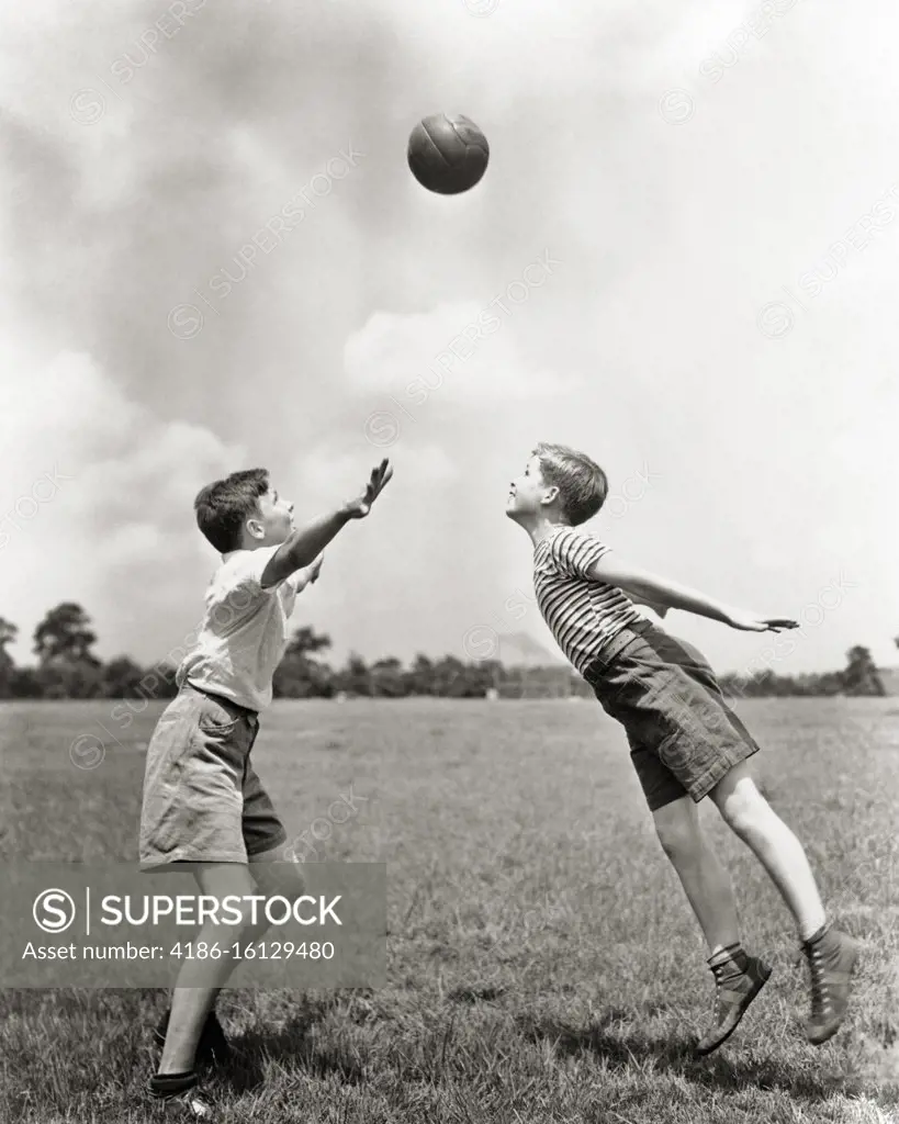 1930s TWO BOYS IN GRASS PLAYING SOCCER BALL IN AIR BETWEEN THEM