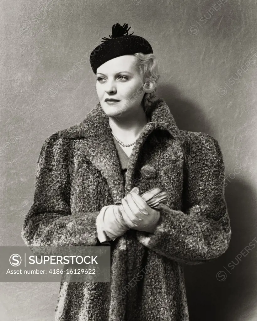 1930s 1940s UNSMILING BLONDE WOMAN WEARING BLACK PILLBOX STYLE HAT WITH TASSEL AND A GRAY PERSIAN LAMB FUR COAT LEATHER GLOVES