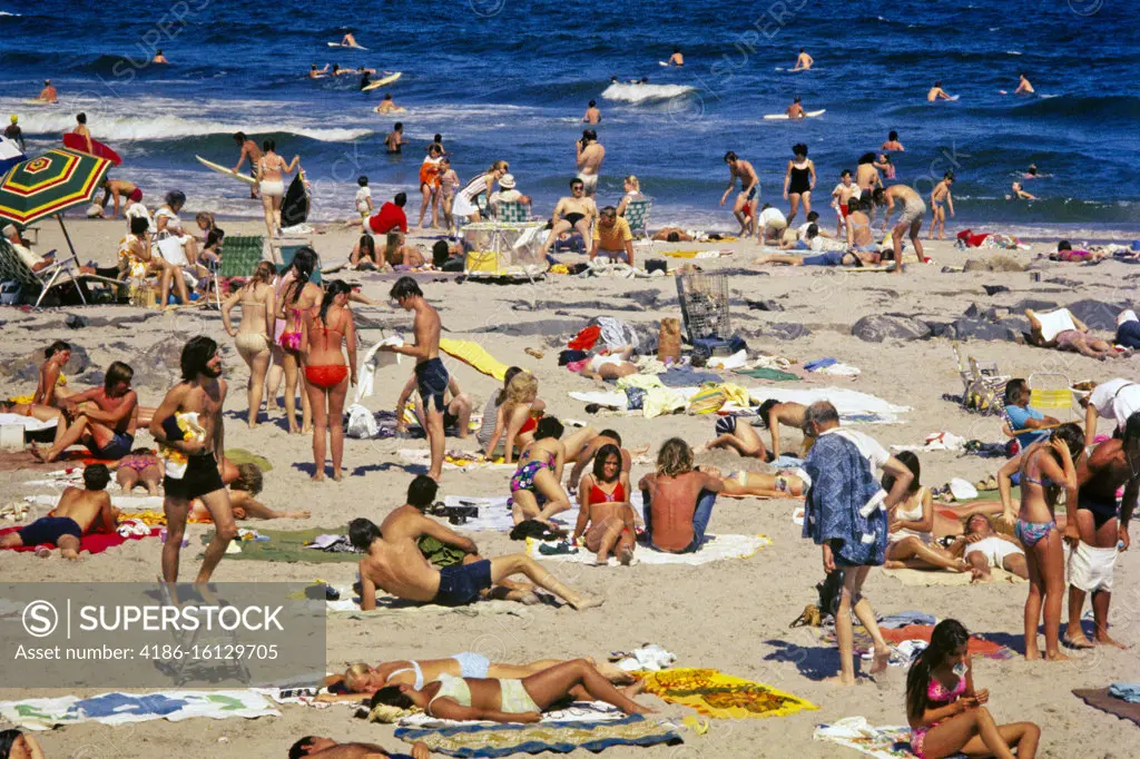 1970s CROWDED BUSY SUMMERTIME BEACH ON JERSEY ATLANTIC OCEAN SHORE BODY SURFERS SUNBATHERS FAMILY GROUPS TEENAGERS NJ USA