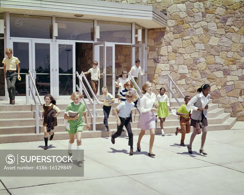 1960s 1970s GROUP OF ETHNICALLY DIVERSE KIDS RUNNING OUT OF SCHOOL BUILDING AT END OF DAY OR END OF SCHOOL YEAR SUMMER BREAK