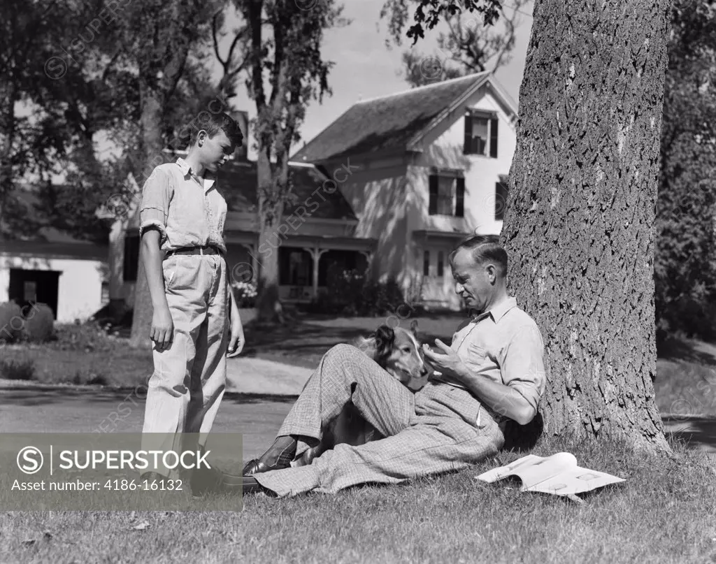 1940S Father And Dog Sitting Under Tree Teenage Son Standing Front Yard Houses Street Community