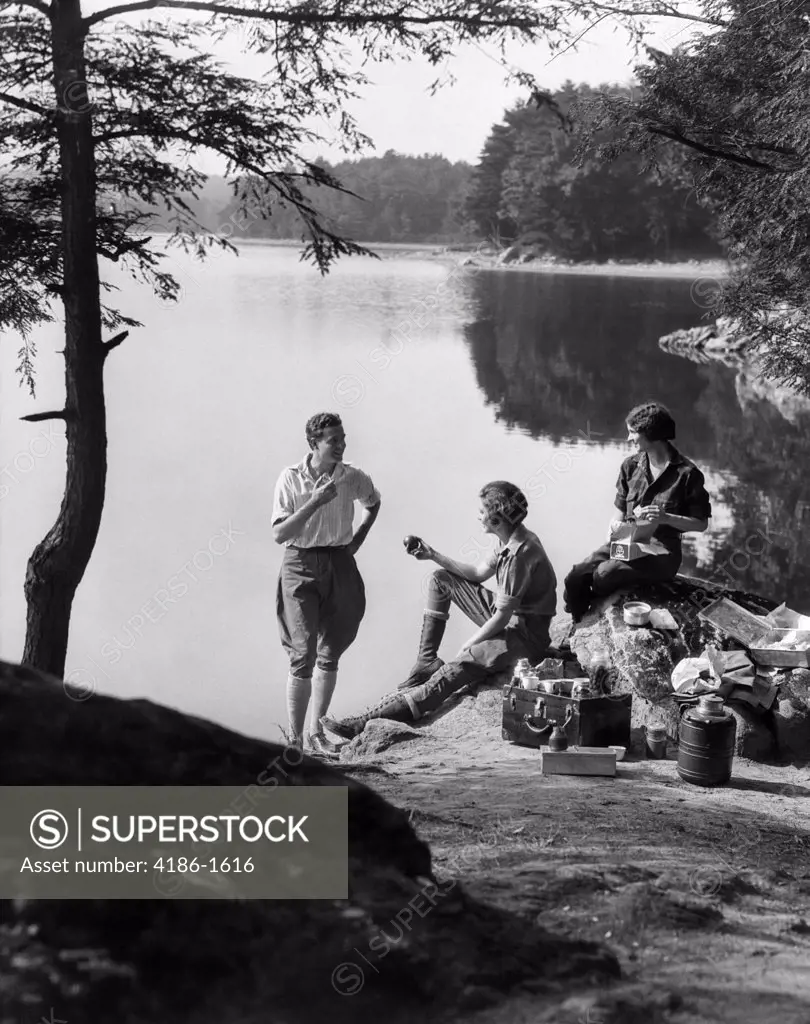 1920S 1930S 3 People Picnicking By Lake Man Wearing Jodhpurs Standing Two Seated Women Berkshires Ma Onata Lake