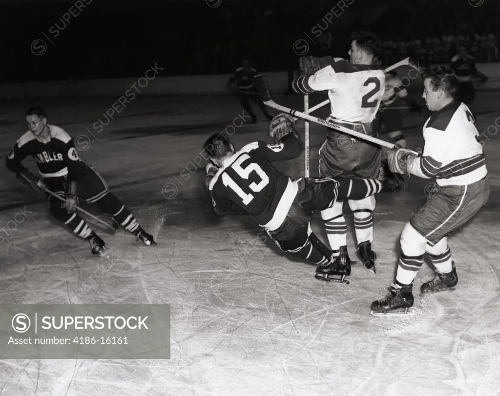 1950S Hockey Game With One Of 4 Players In Foreground Being Knocked Down By 2 Opposing Team Members