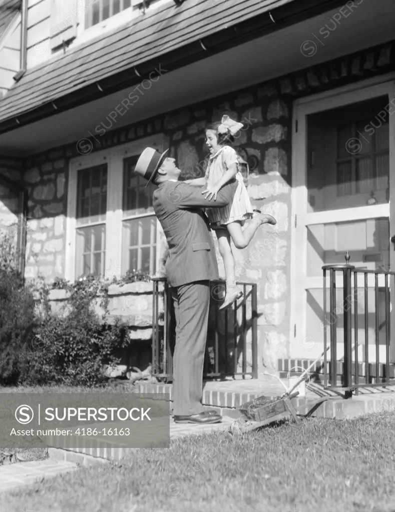 1930S Returning Father Lifting Up Laughing Daughter In Front Of Stone Suburban House