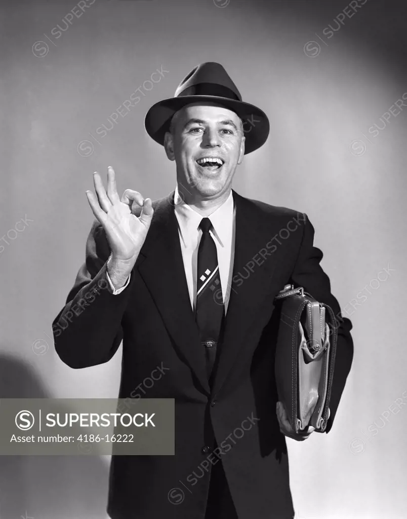 1950S Salesman Man Making Okay Sign With Thumb And Index Finger Carrying Briefcase Wearing Suit Tie And Hat Eager Smiling
