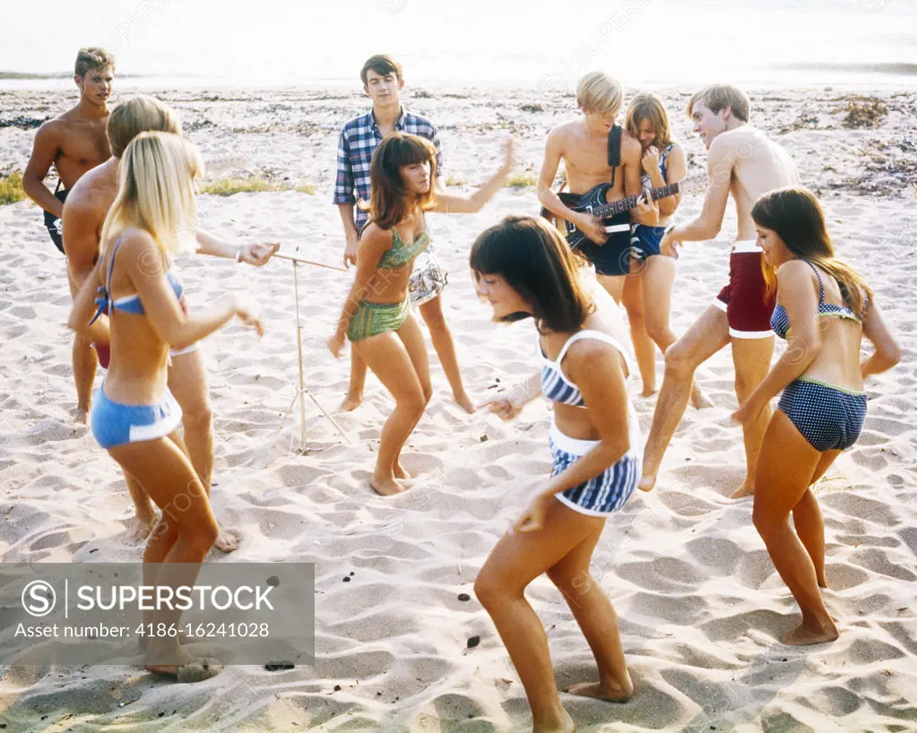 1960s 1970s ANONYMOUS BAND TEENAGE MUSICIANS AND COUPLES BOYS AND GIRLS  WEARING BATHING SUITS DANCING TOGETHER AT A BEACH PARTY - SuperStock