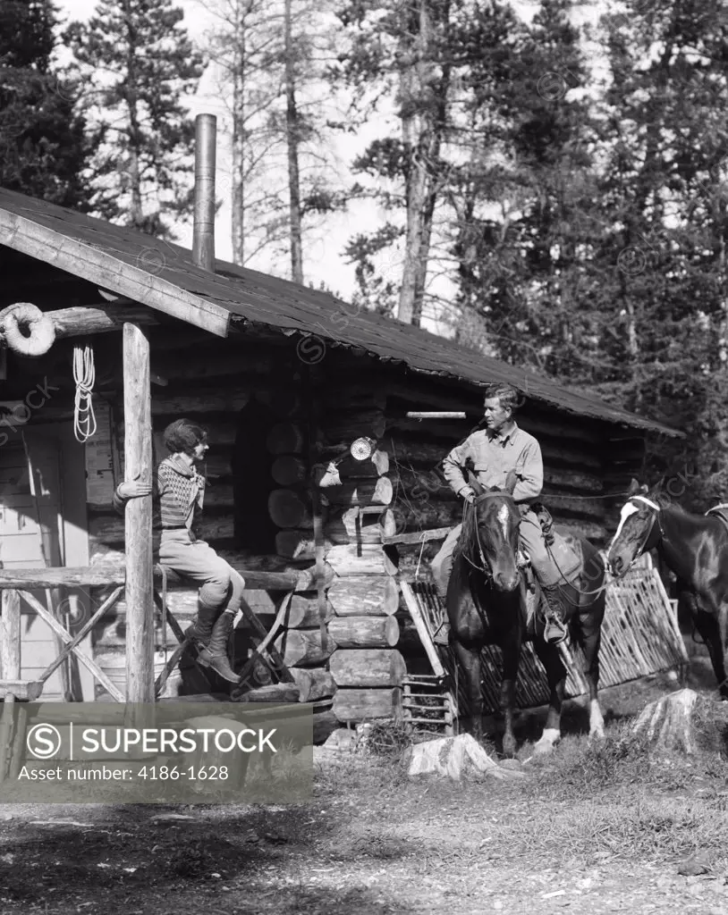 1920S 1930S Couple In Front Of Log Cabin Woman Sitting On Porch Railing Man On Horse Alberta Canada