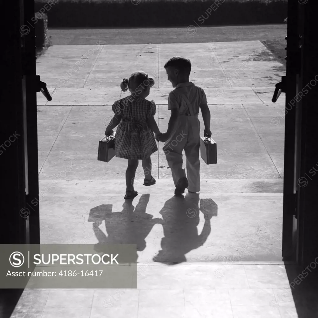 1950S Silhouetted Boy Girl Holding Hands Leaving School Doors Going Home End Of Day Shadows Afternoon Friends Friendship