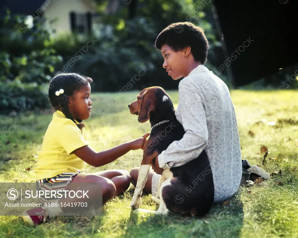 1970s 1980s SERIOUS AFRICAN-AMERICAN MOTHER TEACHING INSTRUCTING DAUGHTER ABOUT CARING FOR PET HOUND DOG WHILE SITTING IN YARD