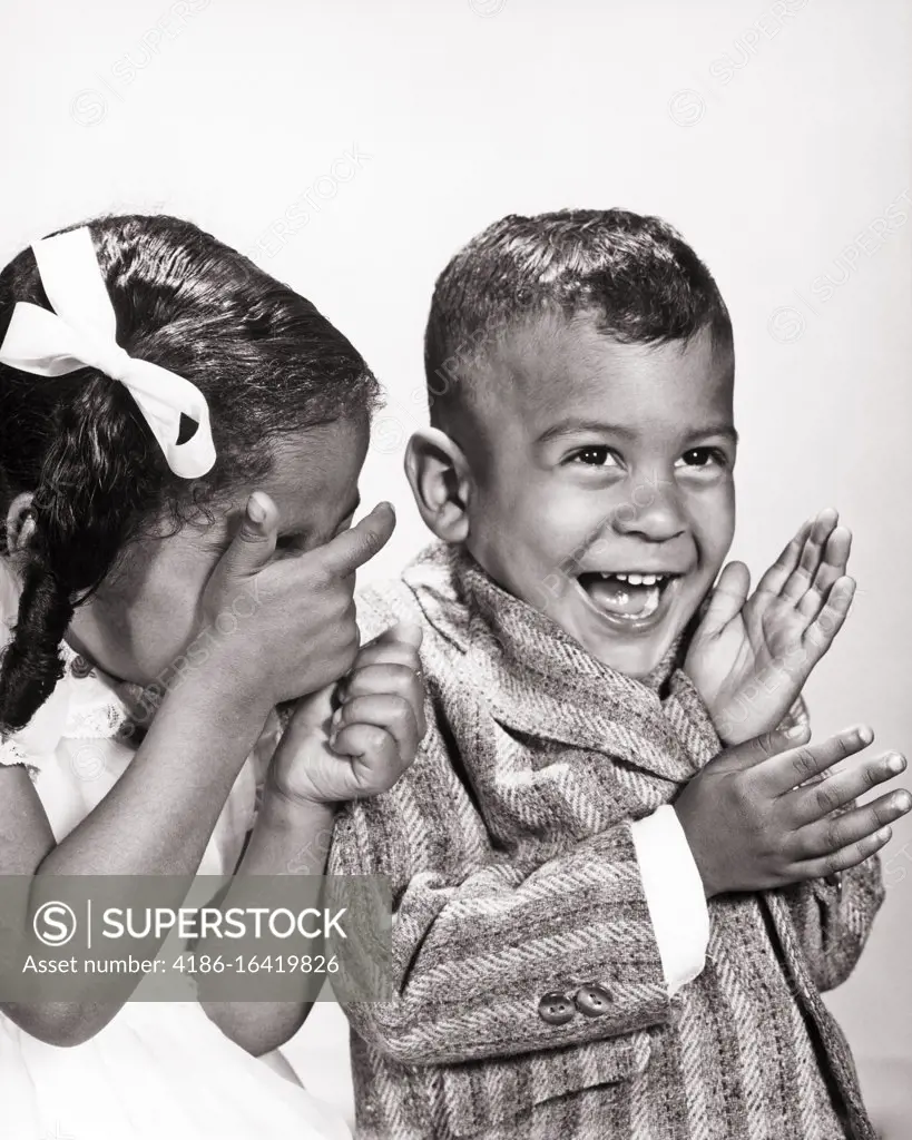 1960s LAUGHING AFRICAN-AMERICAN BOY AND GIRL SHARING A JOKE GIRL HIDING HER EYES
