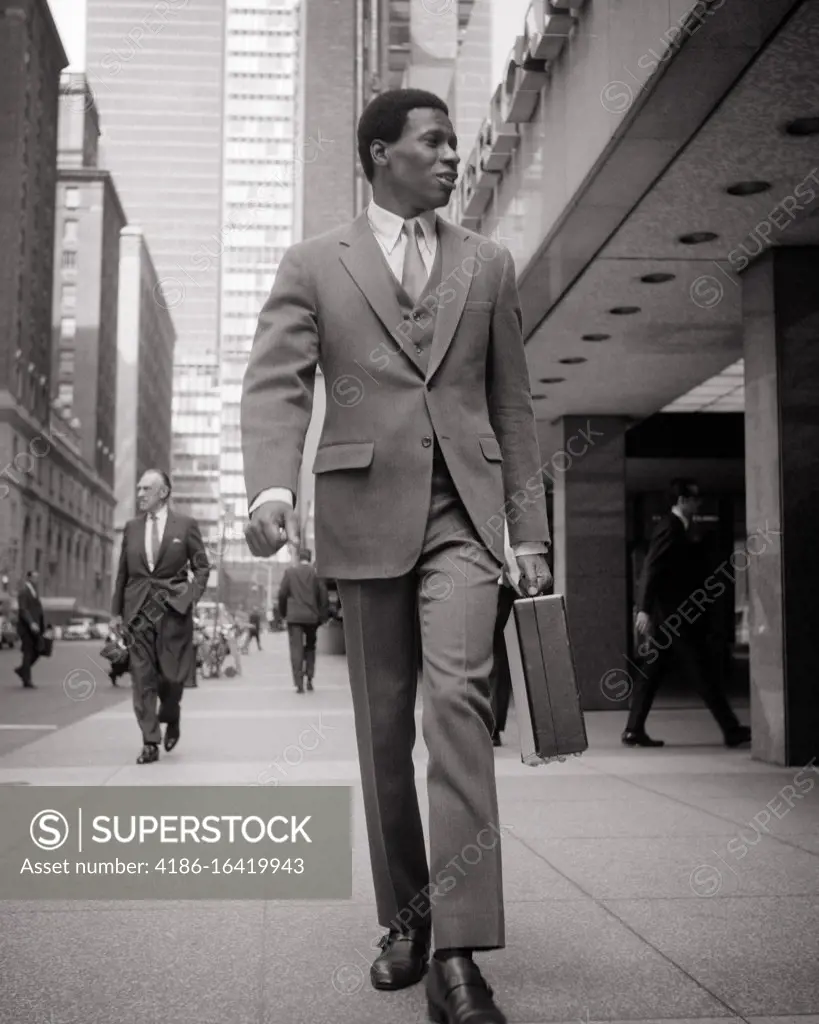 1970s PROFESSIONAL AFRICAN-AMERICAN BUSINESS MAN WALKING ALONG CITY STREET WEARING THREE PIECE SUIT AND TIE CARRYING BRIEFCASE 