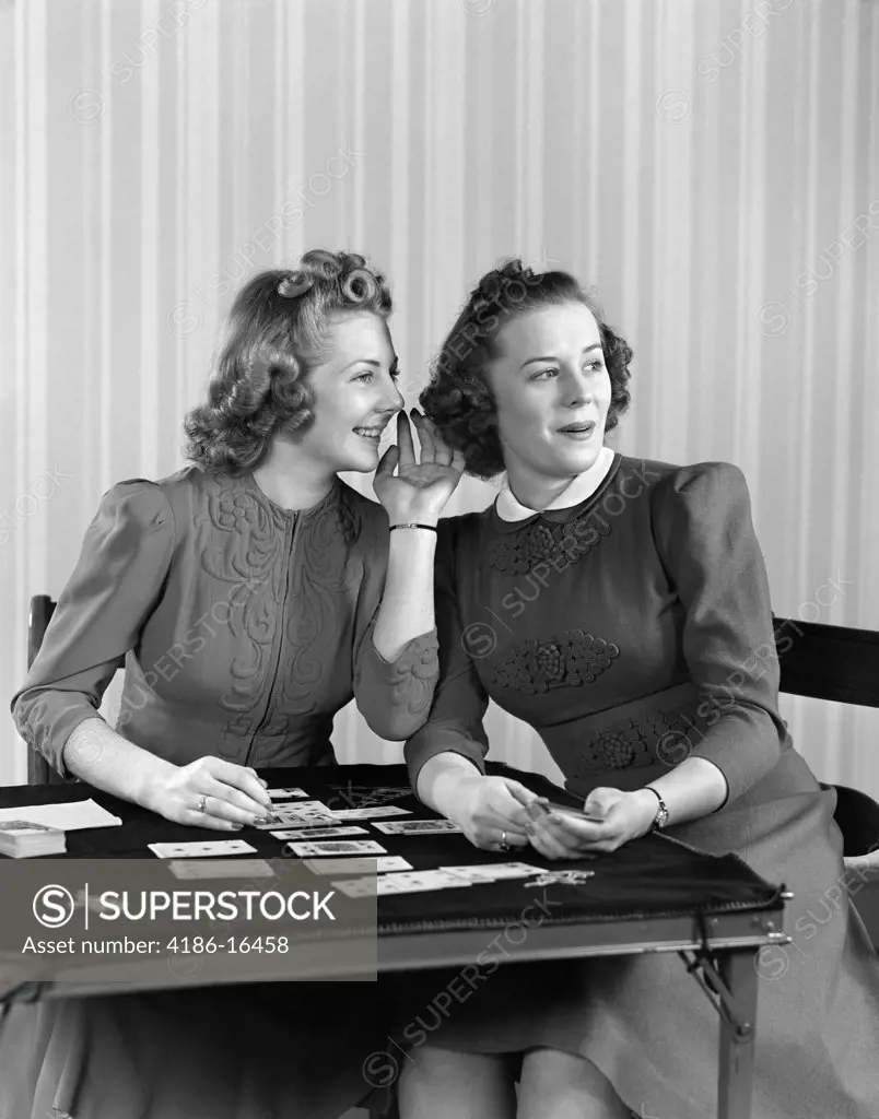 1940S Two Girls Sitting At Card Table Playing Cards And Whispering