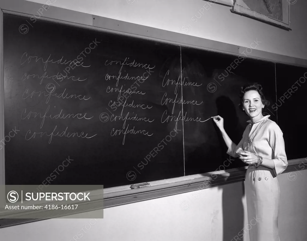 1950S Teacher In Front Of Classroom Writing Confidence On Blackboard