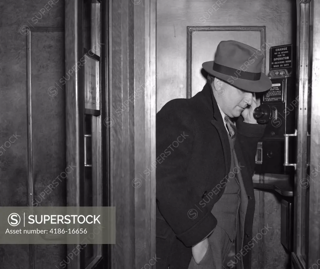 1940S Man Dressed In A Fedora Suit And Overcoat Standing In A Wood Paneled Phone Booth