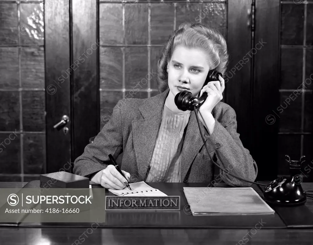 1940S Young Woman Sitting At Information Desk Secretary Talking On Telephone Writing