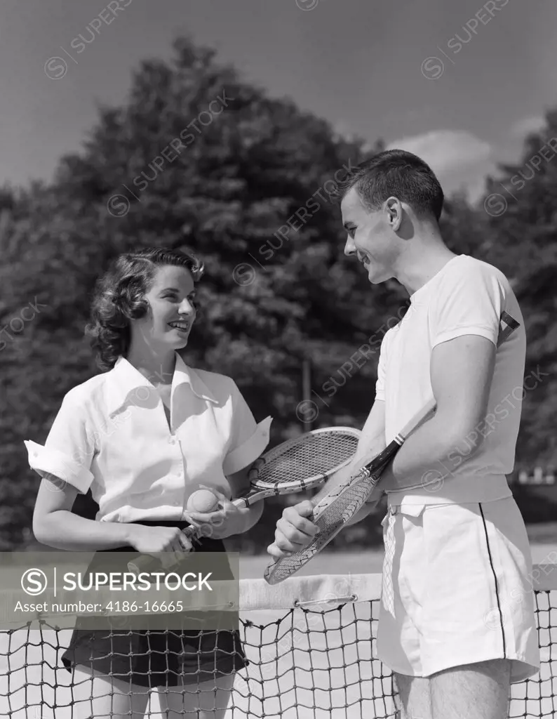 1950S Couple Standing On Opposite Sides Of Net Holding Racquets & Ball & Talking