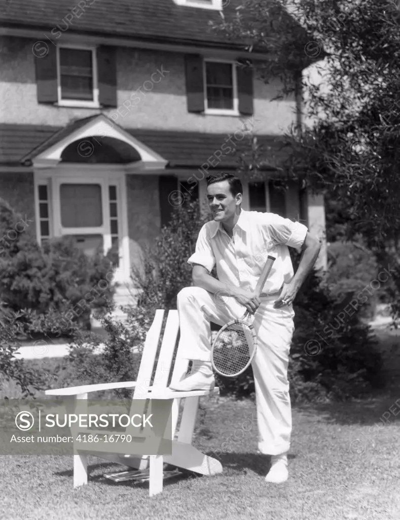 1940S Man In Tennis Whites Holding Racket With Foot On White Adirondack Chair On Lawn