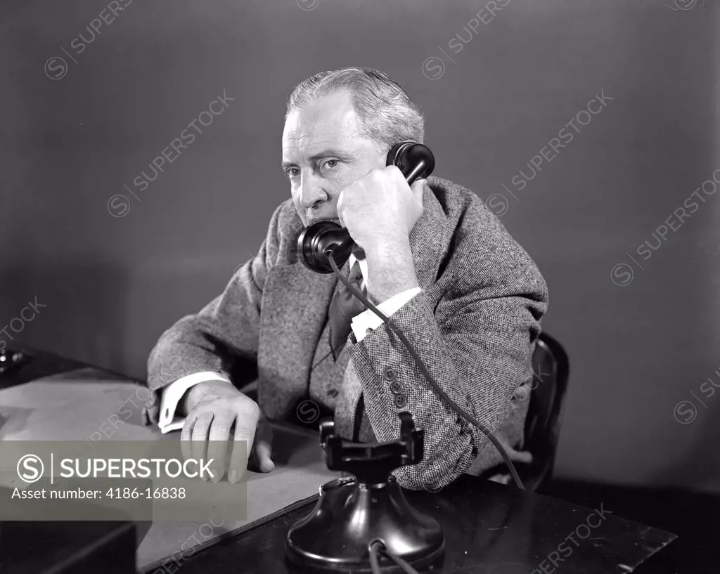 1930S 1940S Suspicious Businessman Talking On Telephone Sitting At Desk