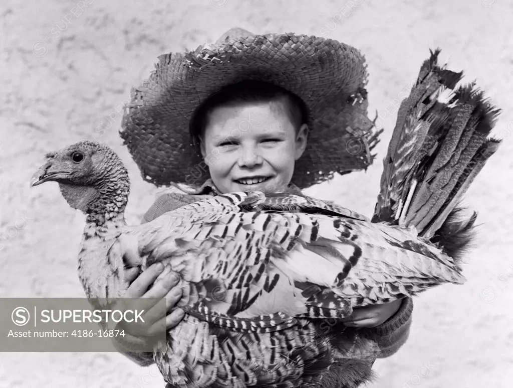 1940S Smiling Boy In Straw Farmer Hat Holding Turkey In Arms Looking At Camera