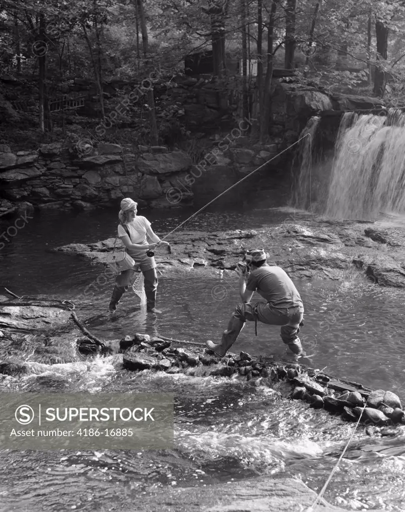 1950S Couple Man Taking Photo Of Woman Fly Fishing In Stream With Waterfall