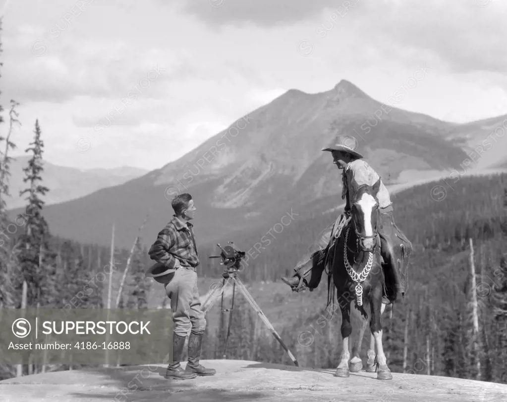 1930S Cameraman In Boots Jodhpurs & Wool Hunting Shirt Standing Next To Movie Camera On Tripod Talking To Mounted Cowboy