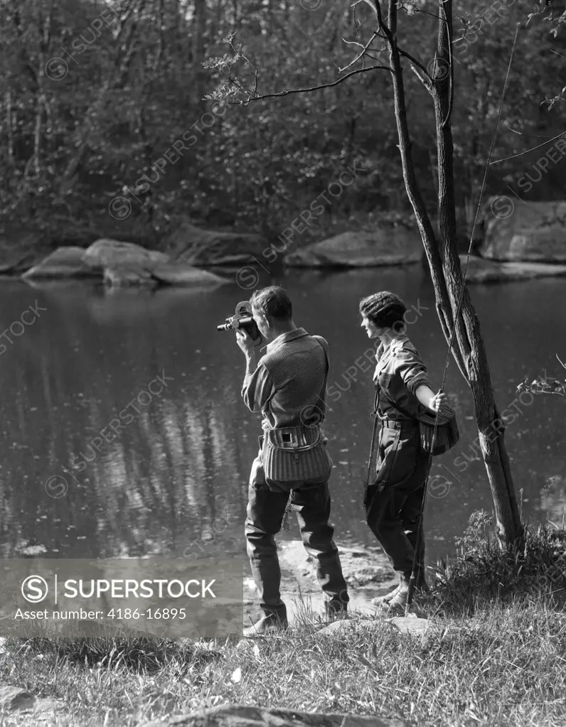 1930S Man With Movie Camera & Woman With Trout Fishing Rod Both Are Wearing Waders & Wicker Creels