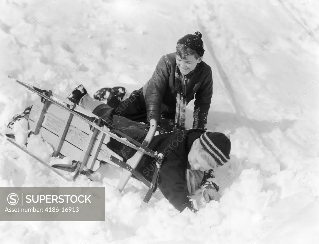 1930S 1940S Two Boys Laughing In Snow Just Fallen Off Of Sled That Is Turned On Its Side