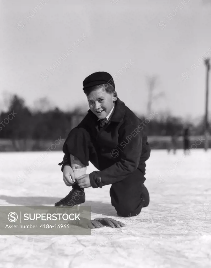 1930S Boy Tying Ice Skate Lace Kneeling On Ice Looking At Camera