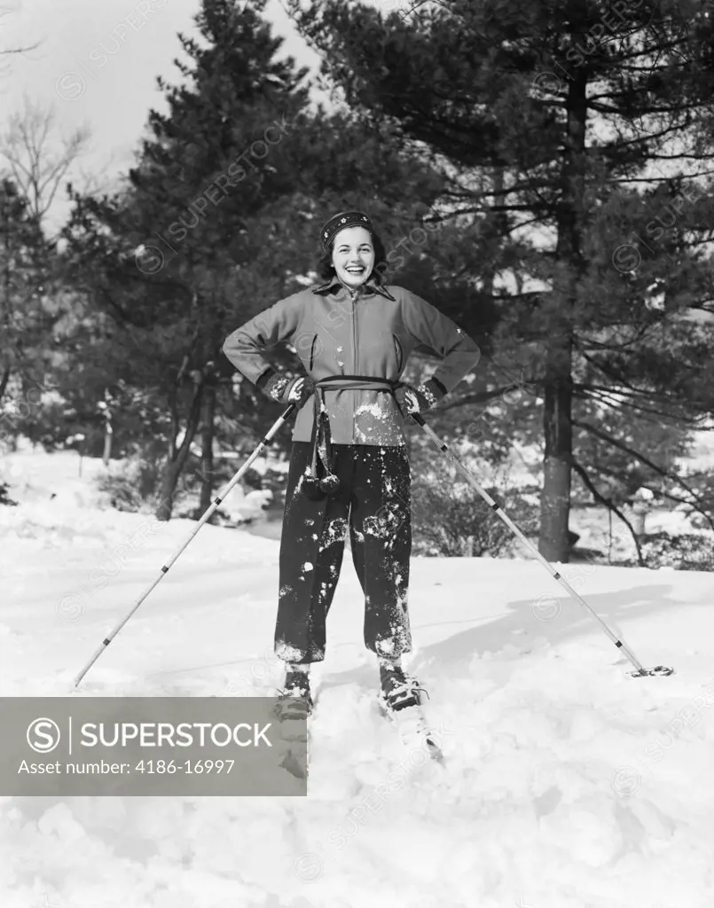 1960S Smiling Woman On Skis Hands On Hips Holding Ski Poles On Ski Slope In Crisp Fresh Snow