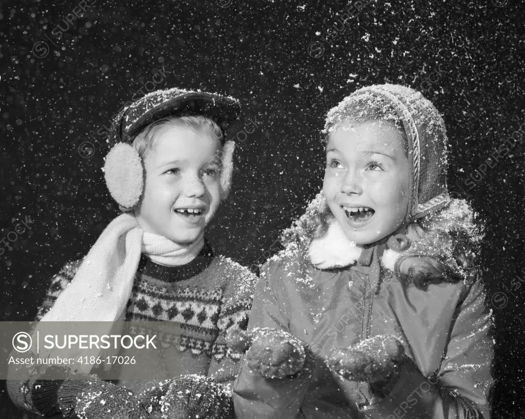 1950S Boy Girl In Winter Dress Hats Gloves Ear Muffs Scarf Smiling Happy Fake Snow Flakes Falling Studio Shot