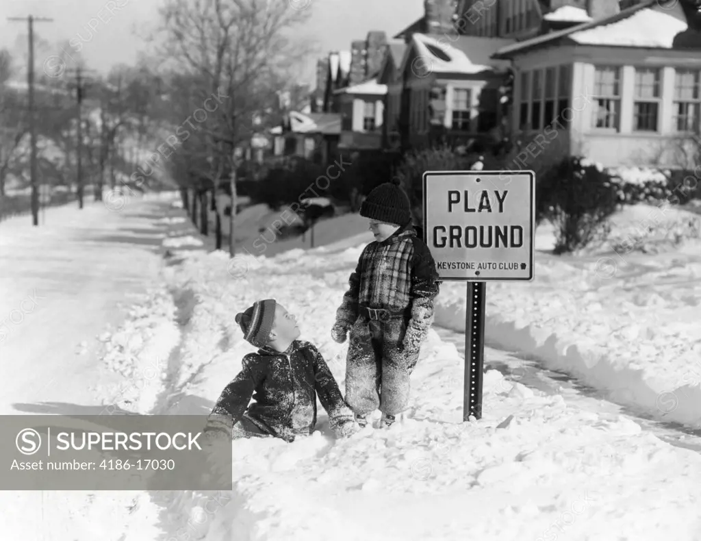 1940S Two Boys Playing In Snowy Suburban Street In Front Of Playground Sign Winter Fun
