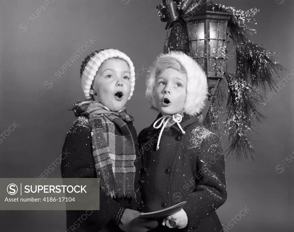 1960S Boy And Girl Singing Christmas Carol Together Under Snowy Outdoor Porch Light