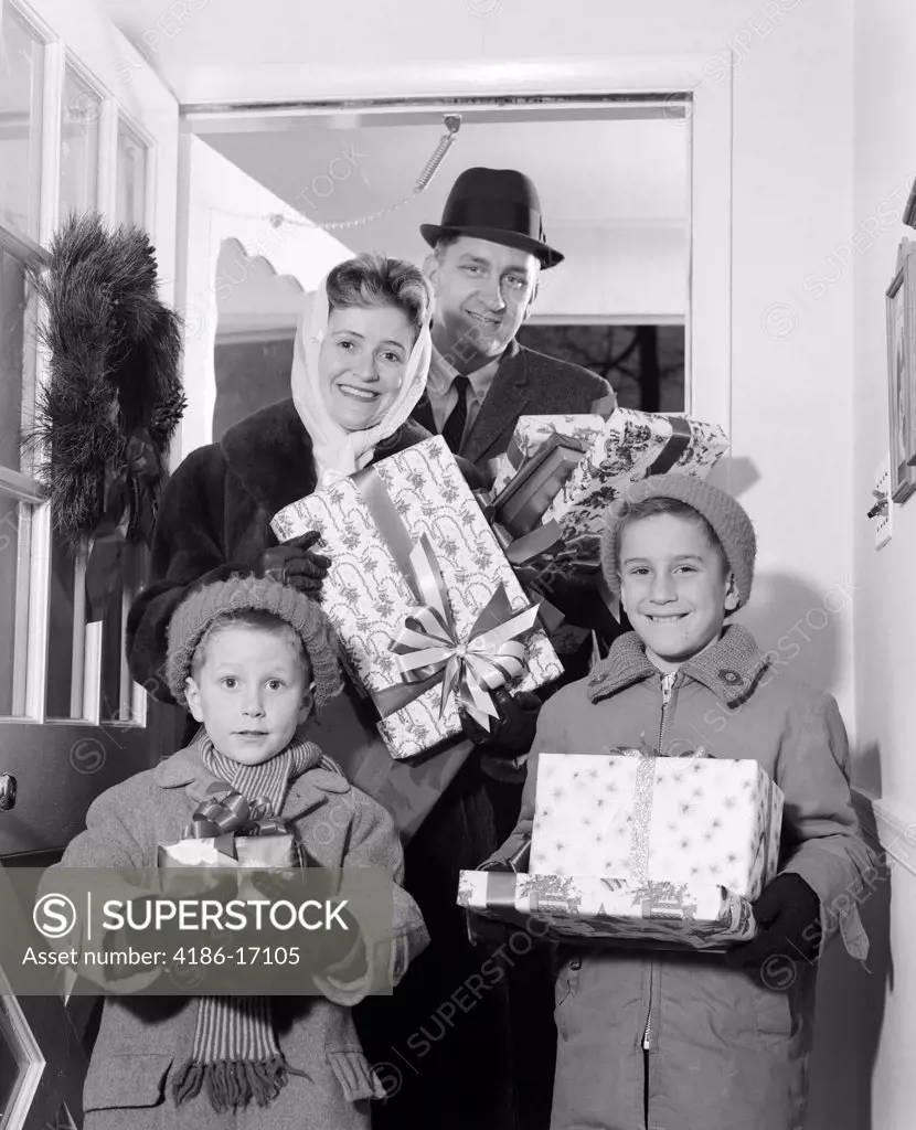 1960S Family Standing In Doorway Of Home Wearing Winter Coats & Hats Holding Wrapped Gifts