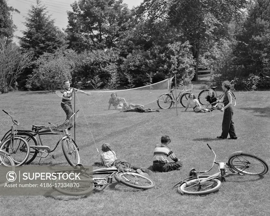 1950s GROUP OF TEENS LYING IN GRASS WITH BICYCLES BOY GIRL PLAYING BADMINTON 
