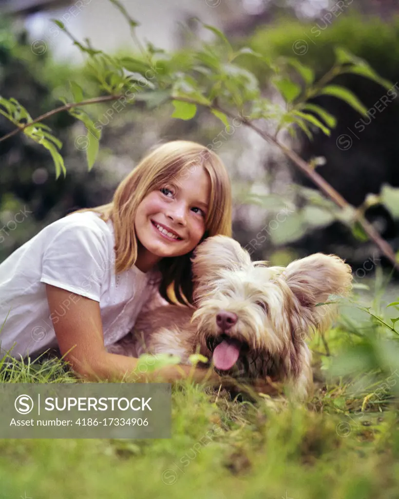 1960s SMILING BLOND GIRL LYING IN GRASS PLAYING WITH HER SHAGGY PET DOG