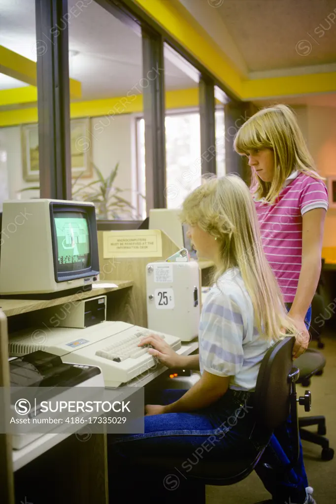 1980s 2 GIRLS WORKING ON COMPUTER IN PUBLIC LIBRARY COMPUTER LAB PAY AS YOU GO VENDING DEVICE